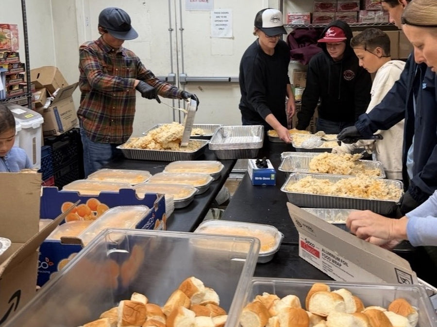 Student volunteers and adults packing Thanksgiving meals of mashed potatoes and dinner rolls in a kitchen