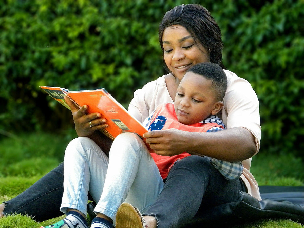 A mother and her young son reading a book together on the grass