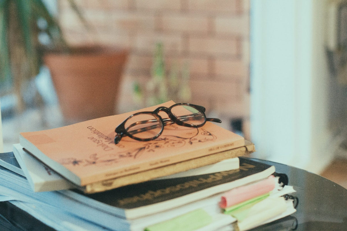 A stack of books with reading glasses on a table